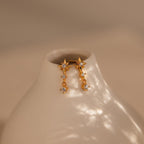 Diamond Starburst Drop Studs—gold star-shaped earrings with dangling crystals—are displayed on a smooth, off-white ceramic vase.