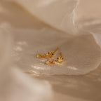 Diamond Starburst Drop Studs in 18K Gold with small crystals rest on soft, beige fabric under gentle lighting, adding a refined touch to any look.