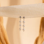 Dainty Pearl Drop Studs featuring three white pearls each, elegantly displayed on a textured cream-colored fabric background.