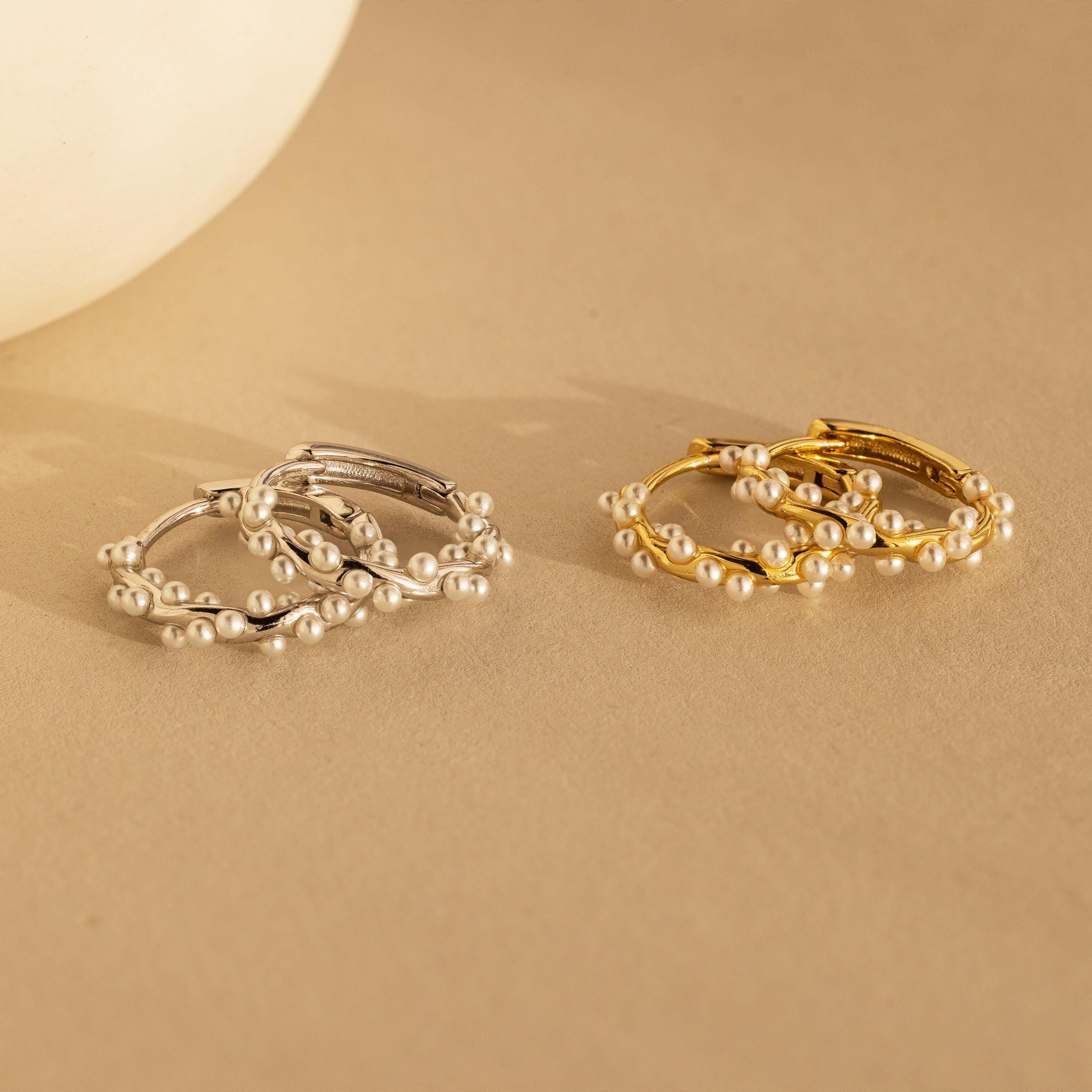 Two pairs of pearl earrings, featuring elegant Pearl Cluster Huggies in Sterling Silver, displayed on a beige surface—ideal as bridal earrings or for any special occasion.