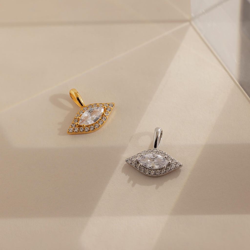 One gold and one silver Pave Evil Eye Charm laying side by side