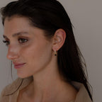 A woman with wet hair faces left against a plain background, wearing Black Diamond Drop Huggies that showcase a small black pendant.