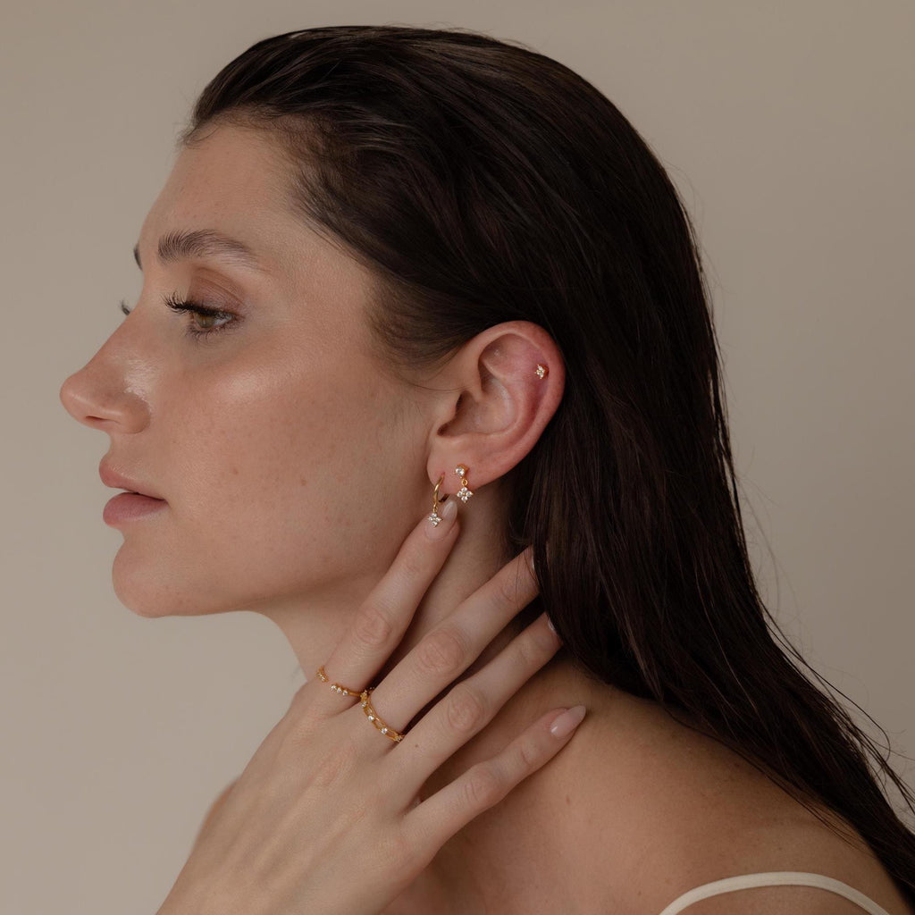 Woman with wet dark hair, wearing gold rings and Ivy Flower Flat Back Studs in Sterling Silver, touching her neck and looking left—an elegant look ideal for a Mother’s Day gift.