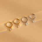 Two pairs of elegant earrings—one gold, one silver—feature a dangling marquise-cut gem, inspired by the Marquise Pave Drop Huggies, and are displayed on a beige surface.
