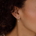 A close-up of a woman's ear wearing Marquise Pave Drop Huggies—delicate silver earrings with a marquise shape and sparkling teardrop gem.