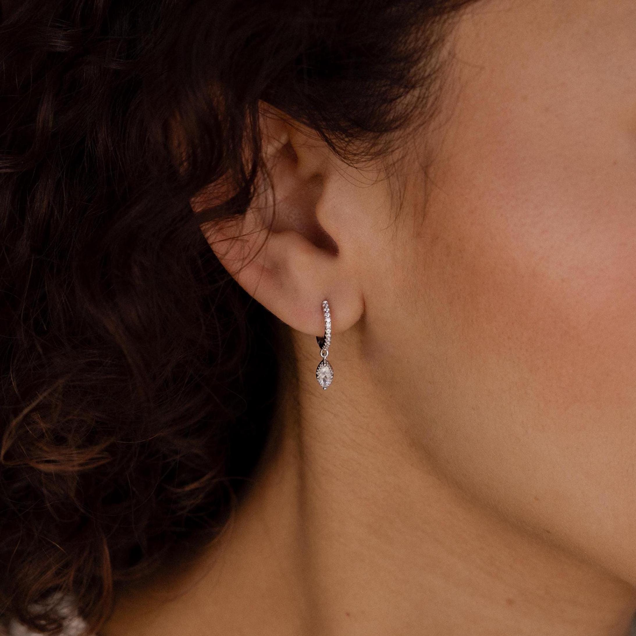 A close-up of a woman's ear wearing Marquise Pave Drop Huggies—delicate silver earrings with a marquise shape and sparkling teardrop gem.