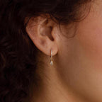 Close-up of a woman's ear wearing Marquise Pave Drop Huggies, with curly hair visible and a delicate gold diamond earring sparkling.