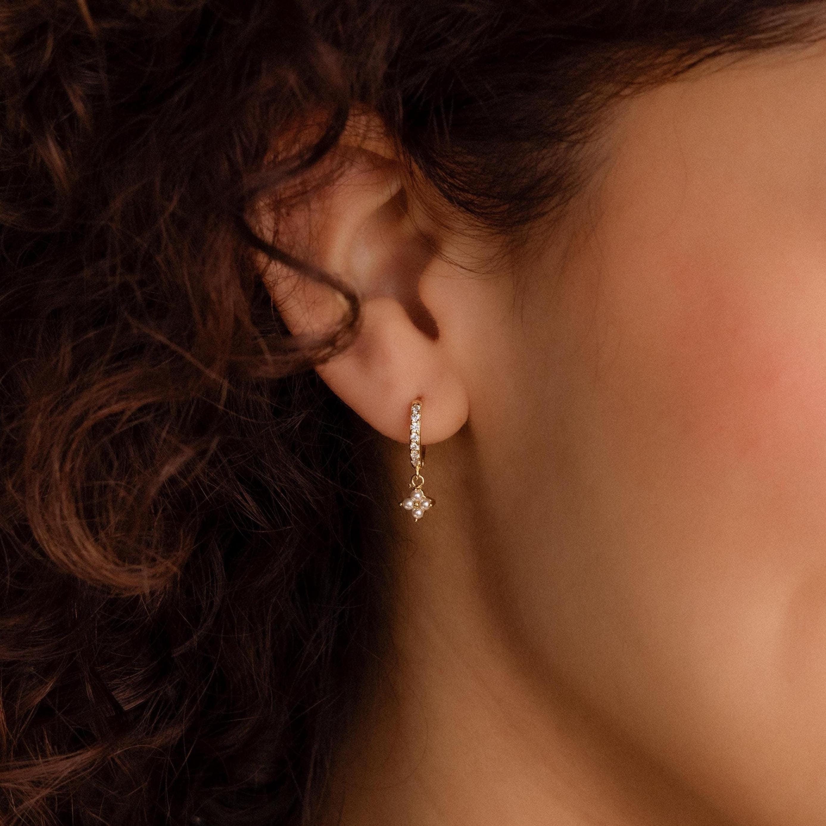 A close-up of a woman's ear with curly hair, wearing Pearl Ivy Flower Huggies that add a touch of sparkle and elegance.