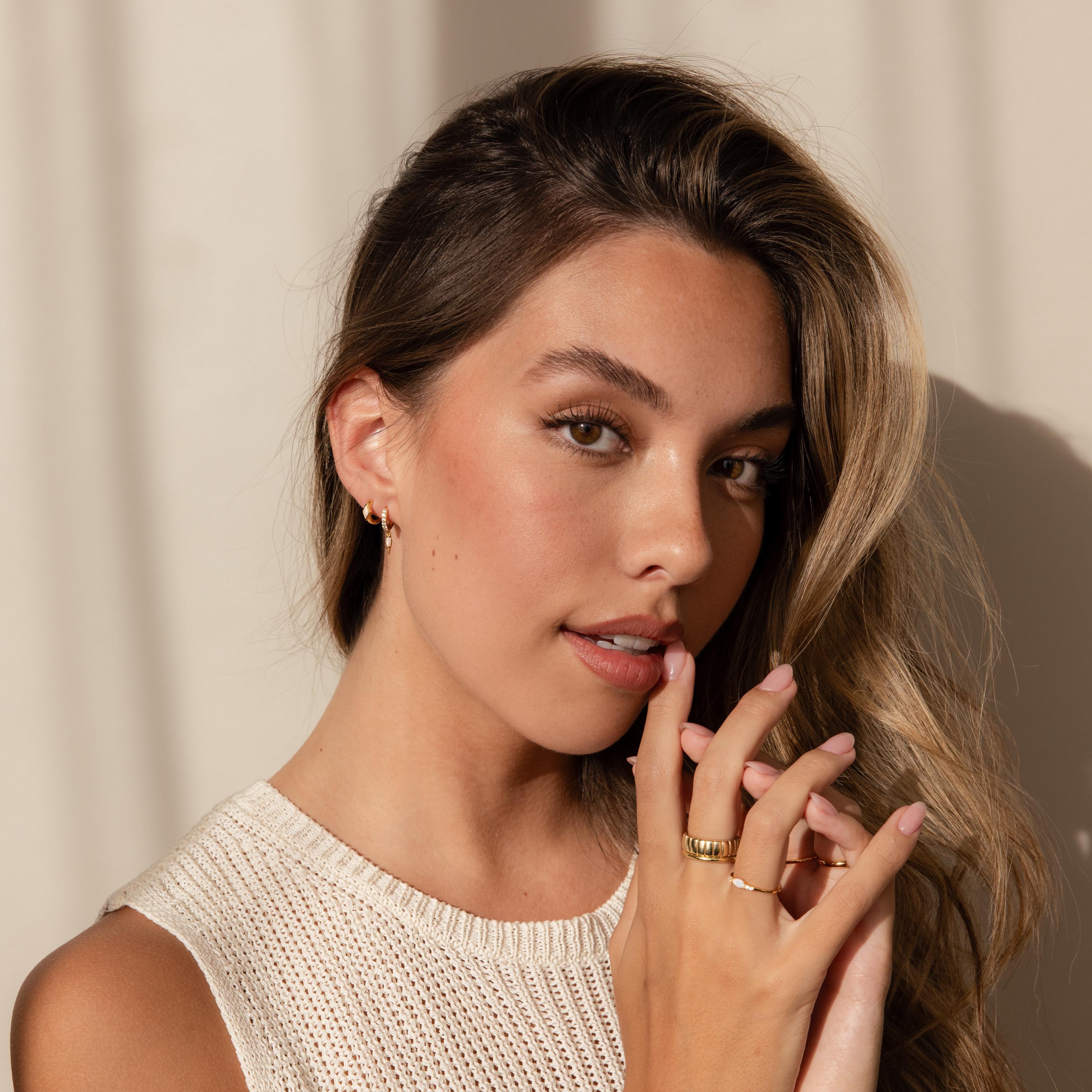 A woman wearing a gold rhombus birthstone huggie and stacking gold rings