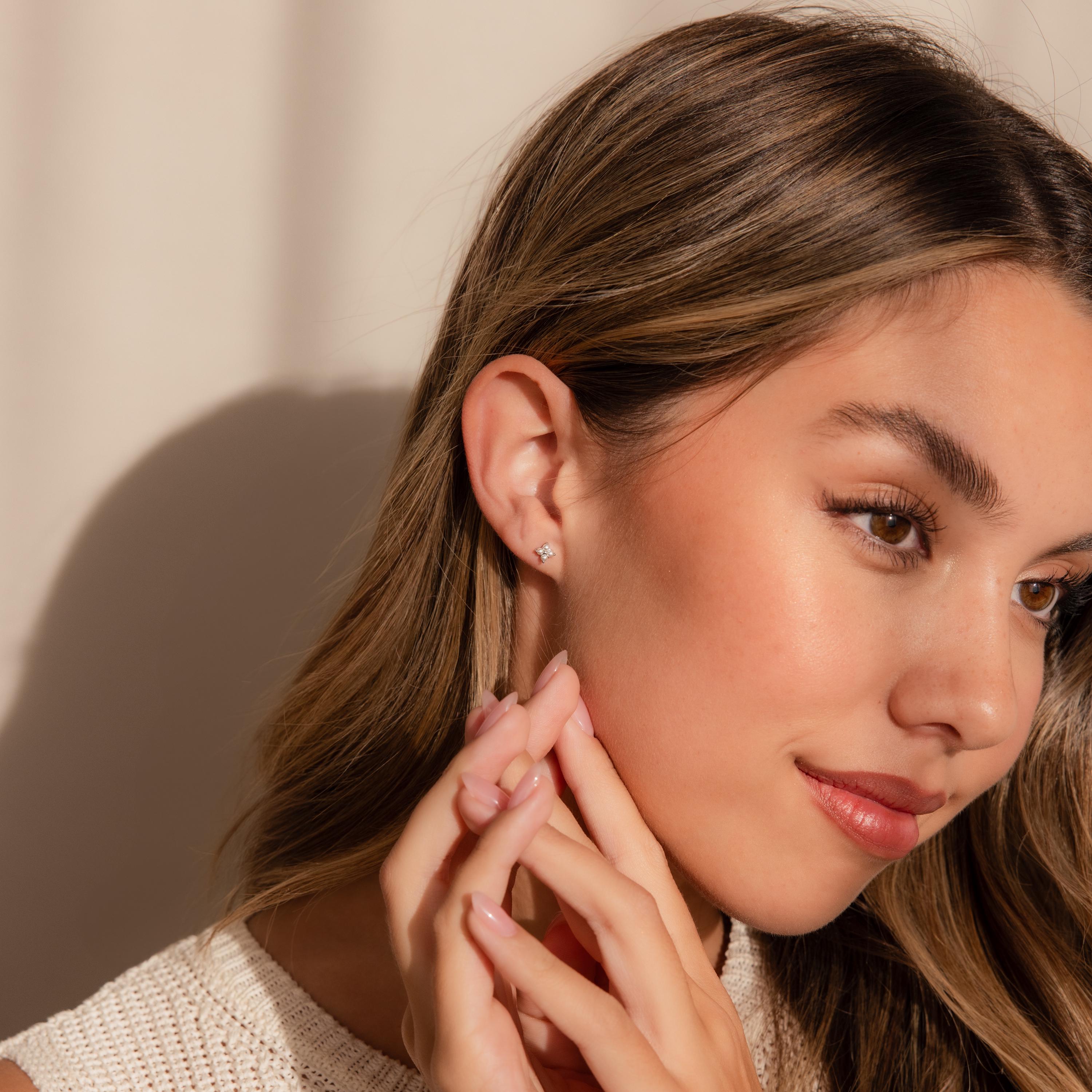 A woman with long brown hair wears Pearl Ivy Flower Studs, gently touching her face while gazing to the side.
