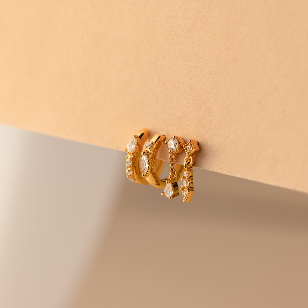 The Dainty Pave Earrings Set features three gold hoop earrings with embedded gemstones, displayed on a beige surface—ideal for adding a delicate touch to your jewelry collection.