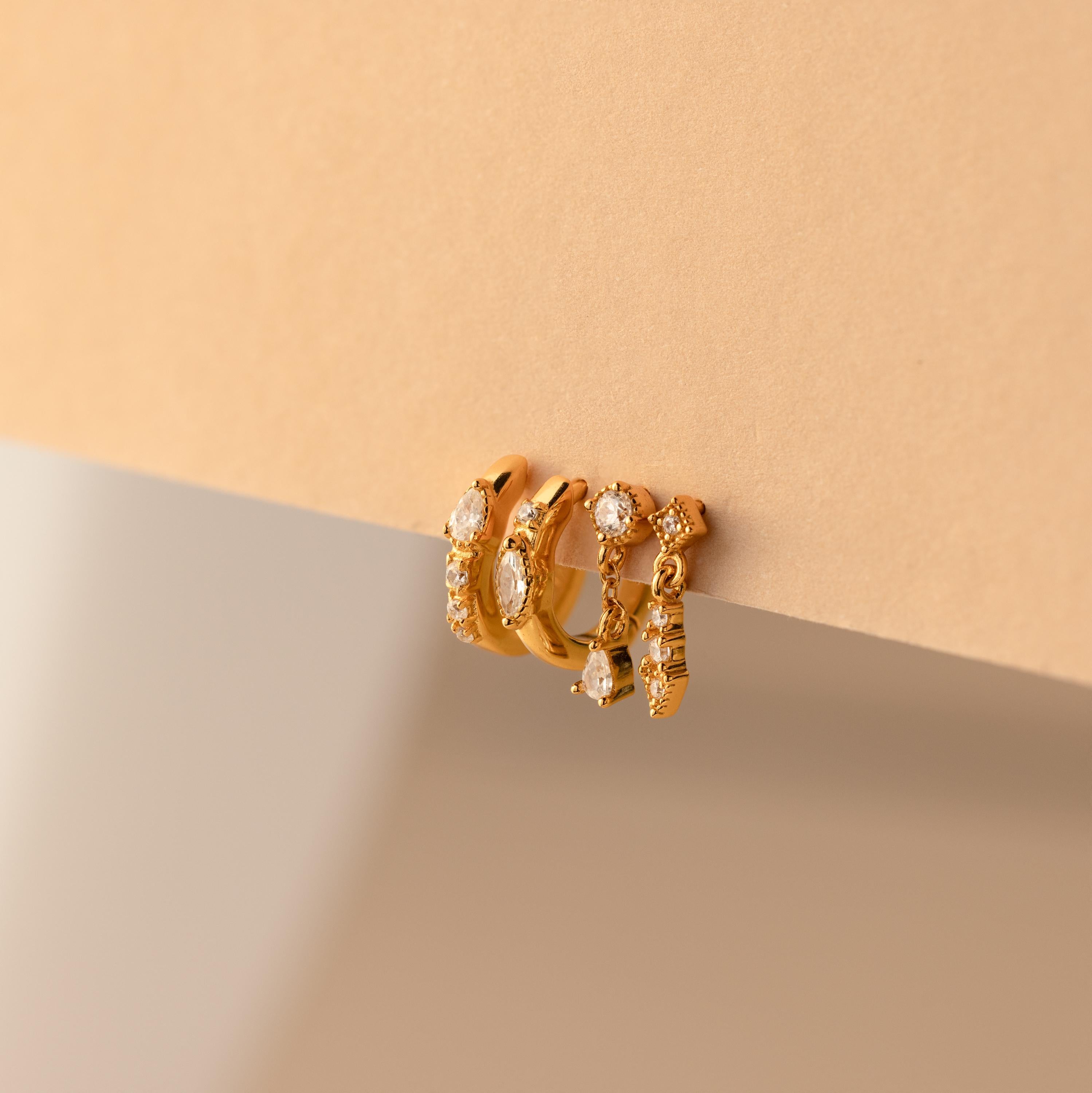 The Dainty Pave Earrings Set features three gold hoop earrings with embedded gemstones, displayed on a beige surface—ideal for adding a delicate touch to your jewelry collection.