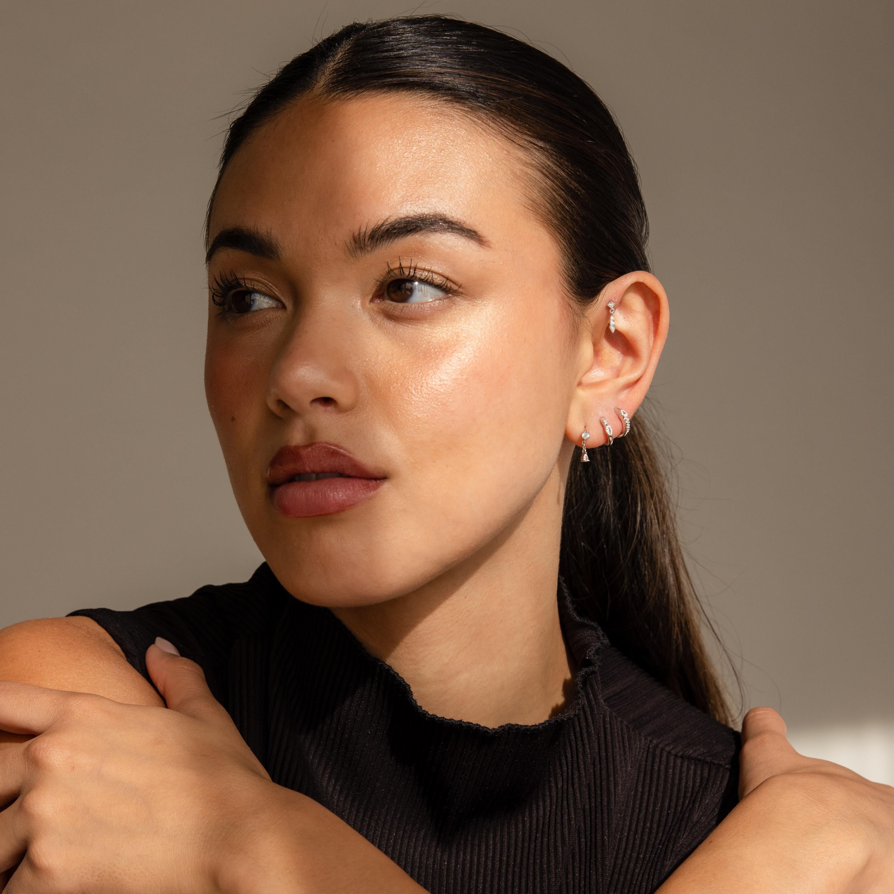 Woman with long dark hair, wearing a sleeveless black top and the Dainty Pave Earrings Set, looking to the side.