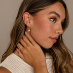 Woman with long brown hair wears Emerald Flatback Studs, touching her neck and looking to the side.