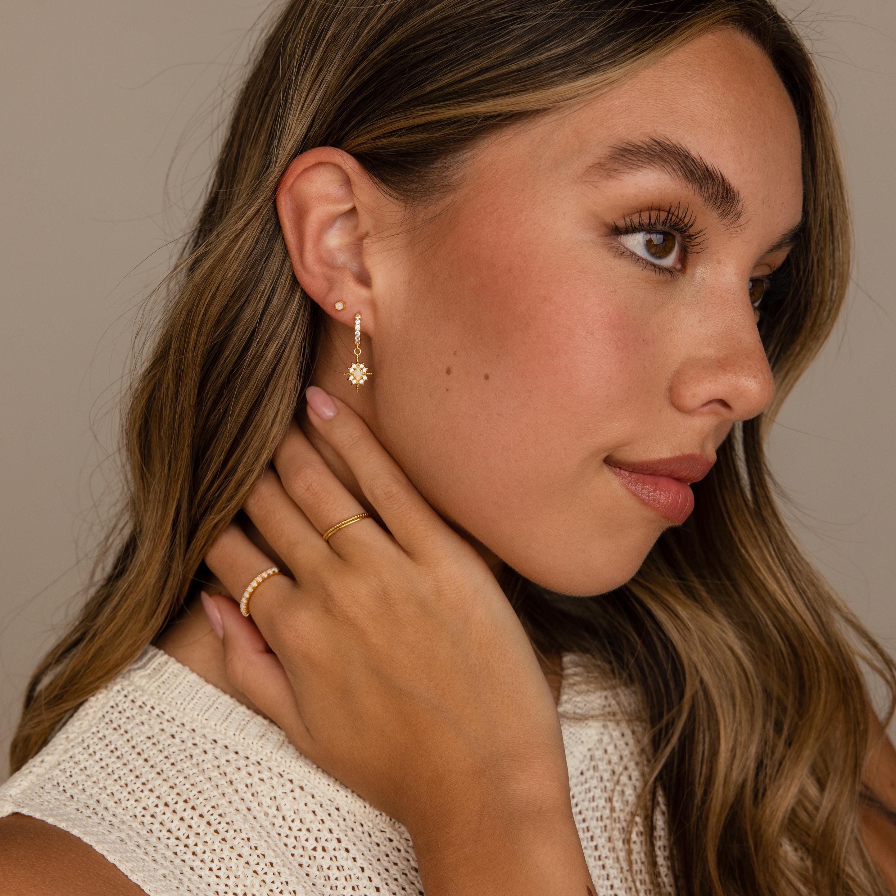 Woman with long brown hair wears Emerald Flatback Studs, touching her neck and looking to the side.