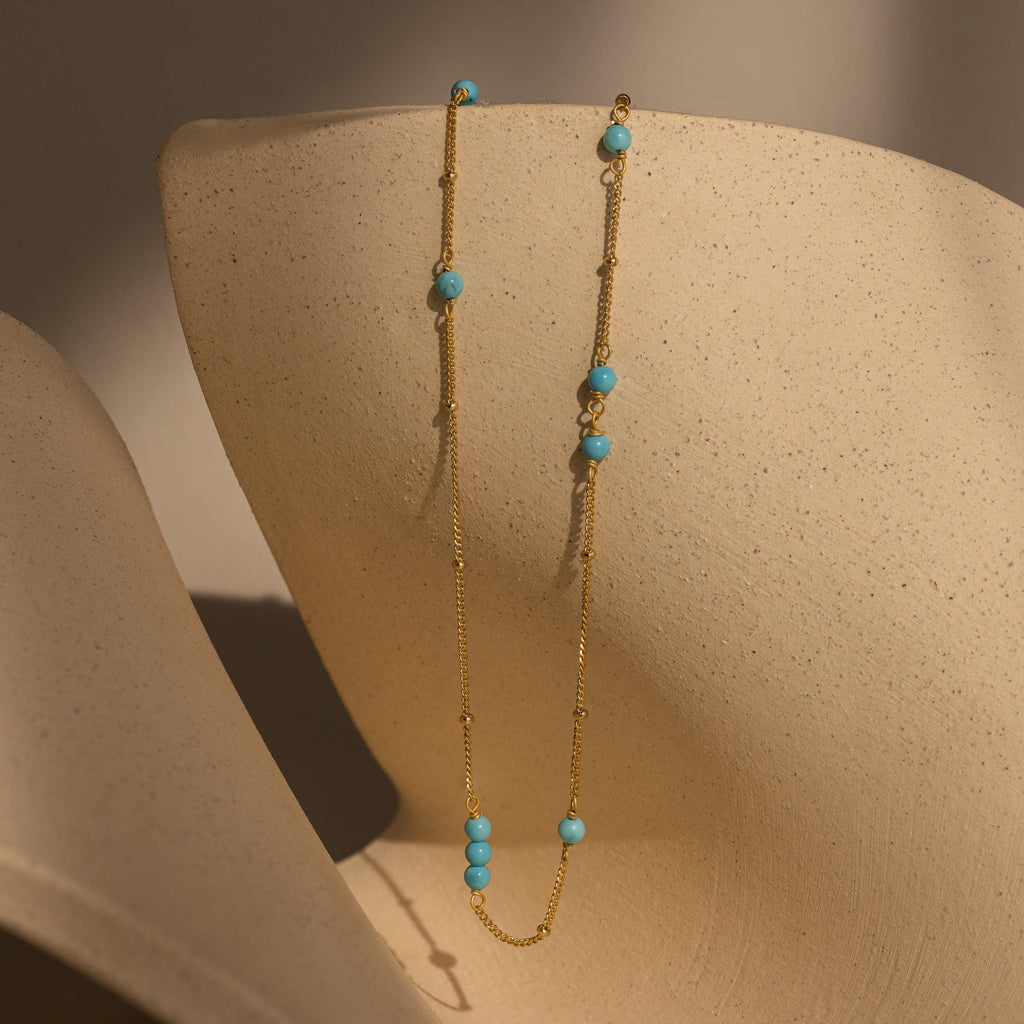 The Turquoise Satellite Necklace features delicate turquoise beads and looks stunning on a beige textured bust with soft shadows—an ideal layering piece for any jewelry collection.
