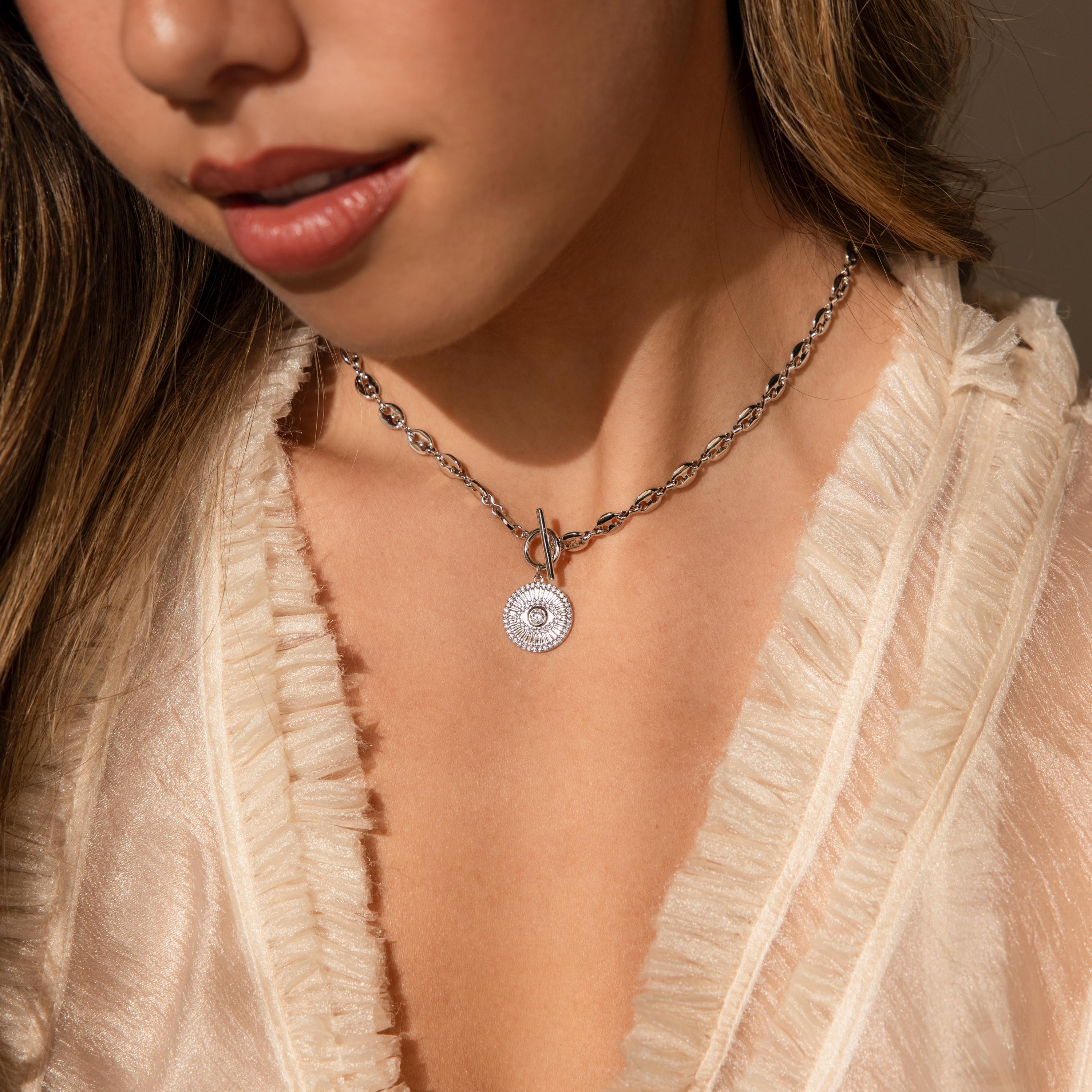 Woman wearing a delicate white ruffled blouse and an Evil Eye Toggle Necklace featuring a circular diamond evil eye charm on a silver mariner chain.