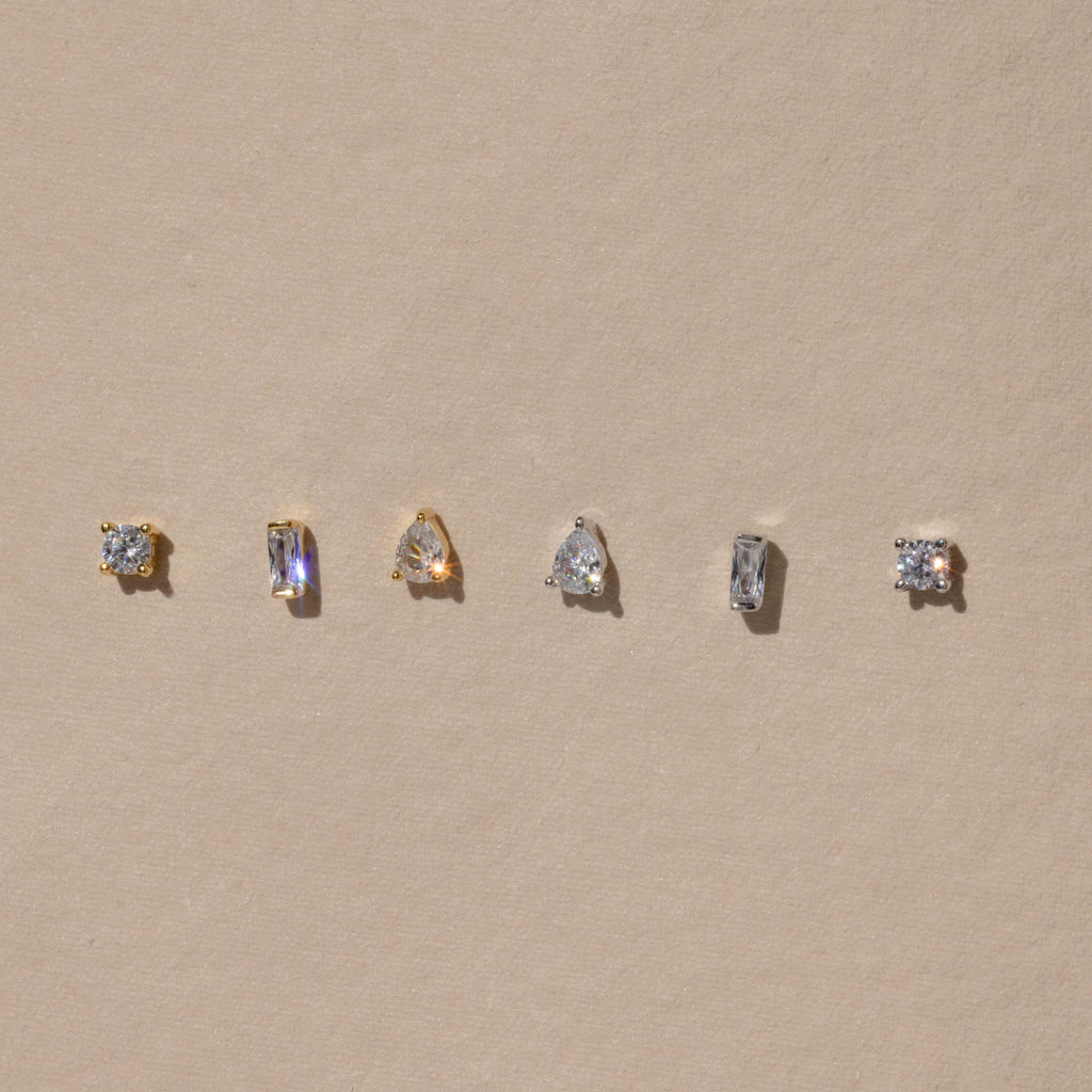 The Mixed Diamond Flat Back Stud Set features five small gold and silver stud earrings, including flat back and mixed diamond designs, displayed in a row on a beige background.