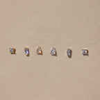 The Mixed Diamond Flat Back Stud Set features five small gold and silver stud earrings, including flat back and mixed diamond designs, displayed in a row on a beige background.
