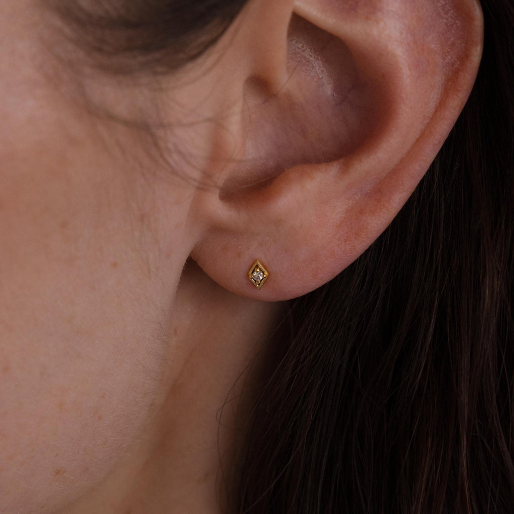 Close-up of a woman’s ear wearing a single gold geometric flat back diamond stud on the earlobe.