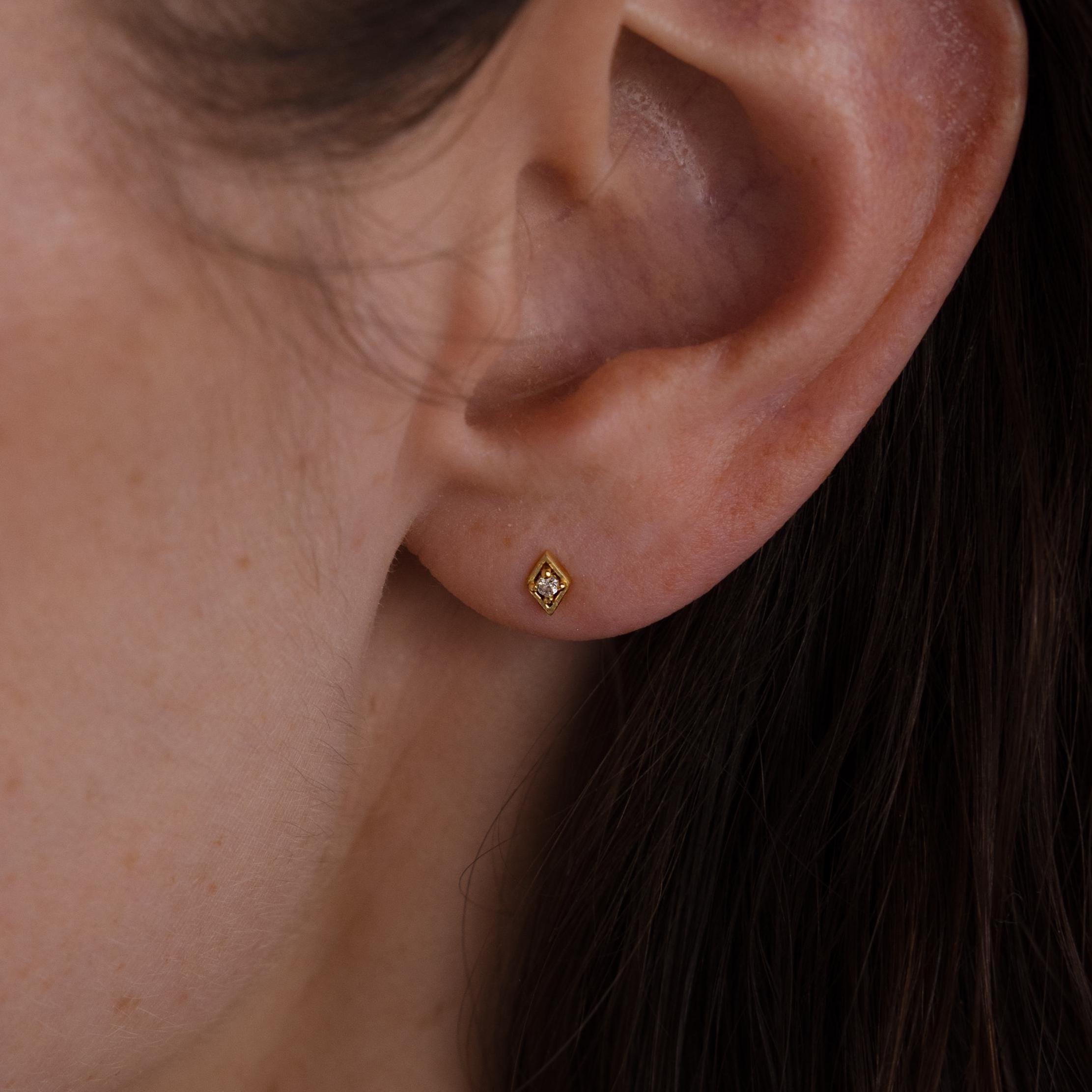 Close-up of a woman’s ear wearing a single gold geometric flat back diamond stud on the earlobe.