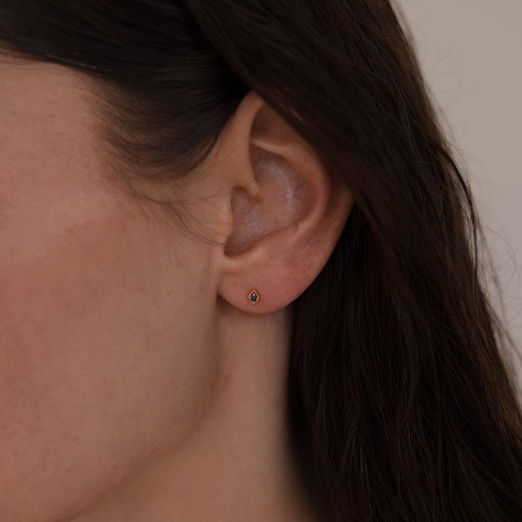 Close-up of a woman wearing a single gold geometric flat back birthstone stud on her earlobe.