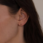 Close-up of a woman wearing a single gold geometric flat back birthstone stud on her earlobe.