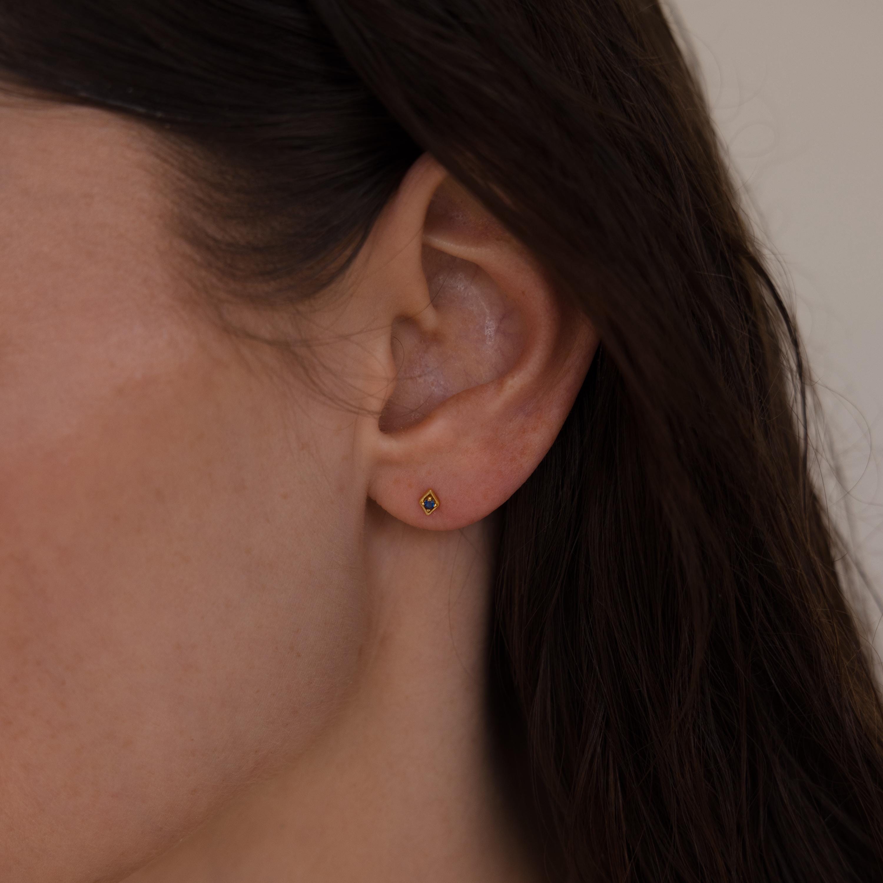 Close-up of a woman wearing a single gold geometric flat back birthstone stud on her earlobe.