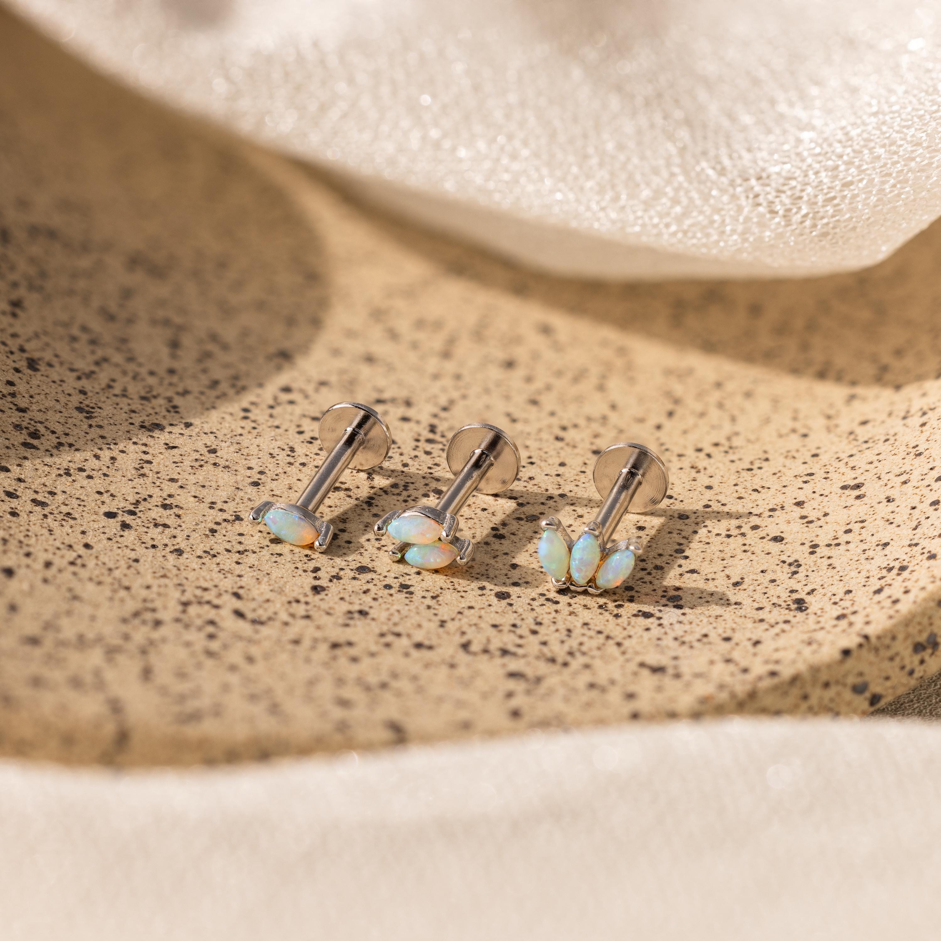 Three pairs of Marquise Opal Flat Back Studs rest on a speckled beige tray with a soft fabric background—an elegant gift for her.