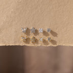 The Pave Assortment Flat Back Set features nine silver and gold pave diamond studs in butterfly, flower, and round designs, beautifully displayed on textured beige paper—an elegant earring set for any occasion.