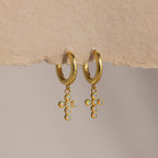 Opal Cross Huggies: gold huggie earrings with iridescent opal cross charms, shown on textured paper.
