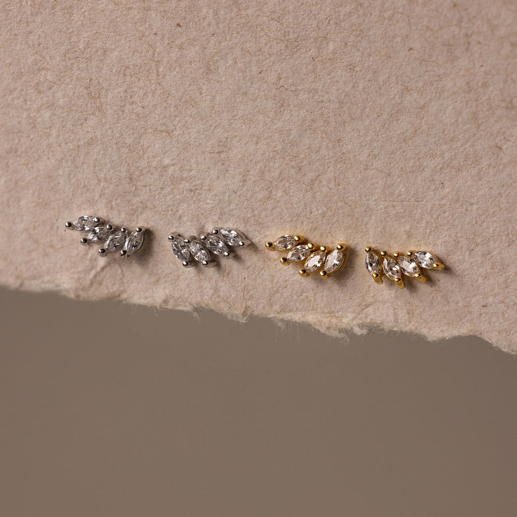 The Marquise Diamond Climbers—two pairs of leaf-shaped stud earrings in silver and gold—evoke wedding jewelry elegance, beautifully displayed on textured beige paper.