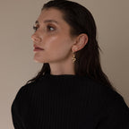 A woman with wet hair wears a black sweater and gold snake-shaped earring, complemented by elegant Marquise Diamond Climbers, as she gazes to the side.