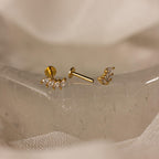 The Marquise Diamond Climbers, elegant gold earrings with shimmering clear stones, are displayed on a translucent crystal against a soft beige background.