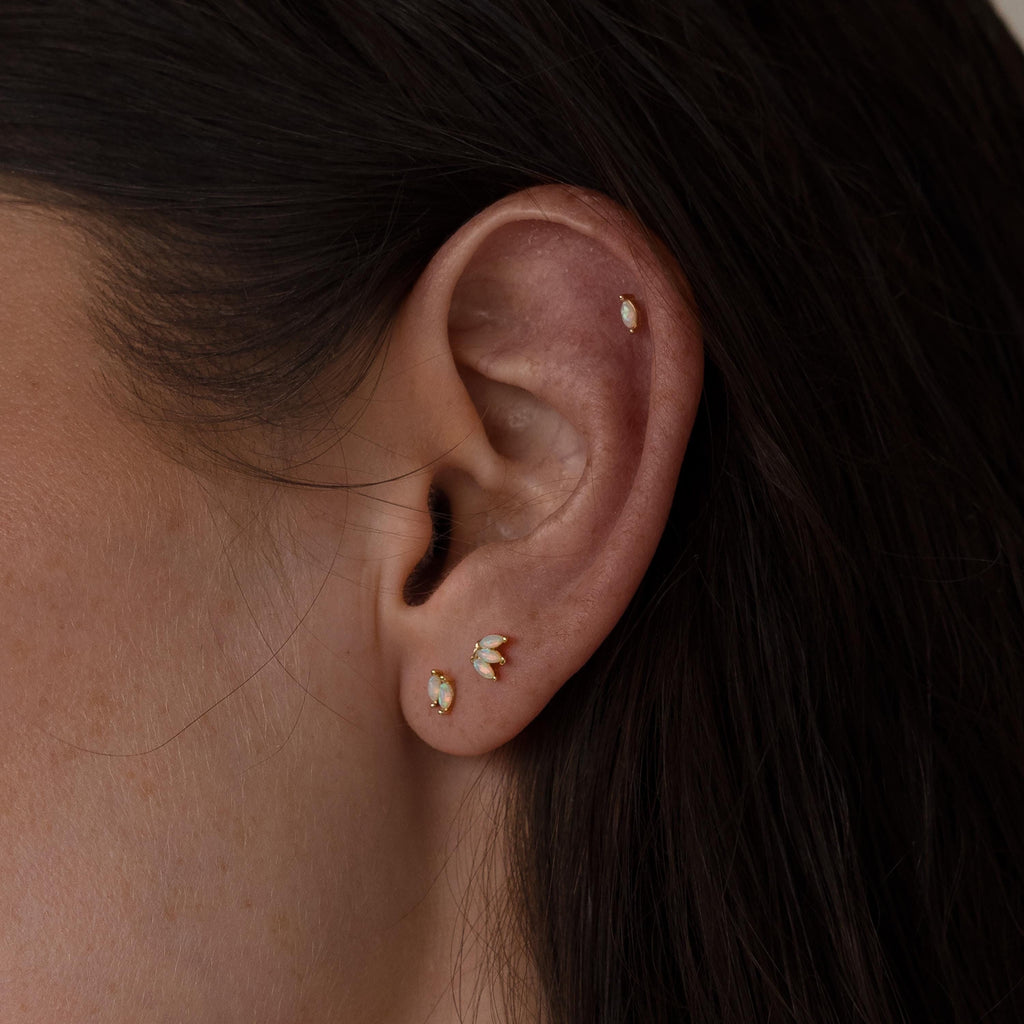 Close-up of a woman's ear with Marquise Opal Flat Back Studs—three gold and white gemstone earrings in the lobe and one in the cartilage, making a perfect Gift for Her.