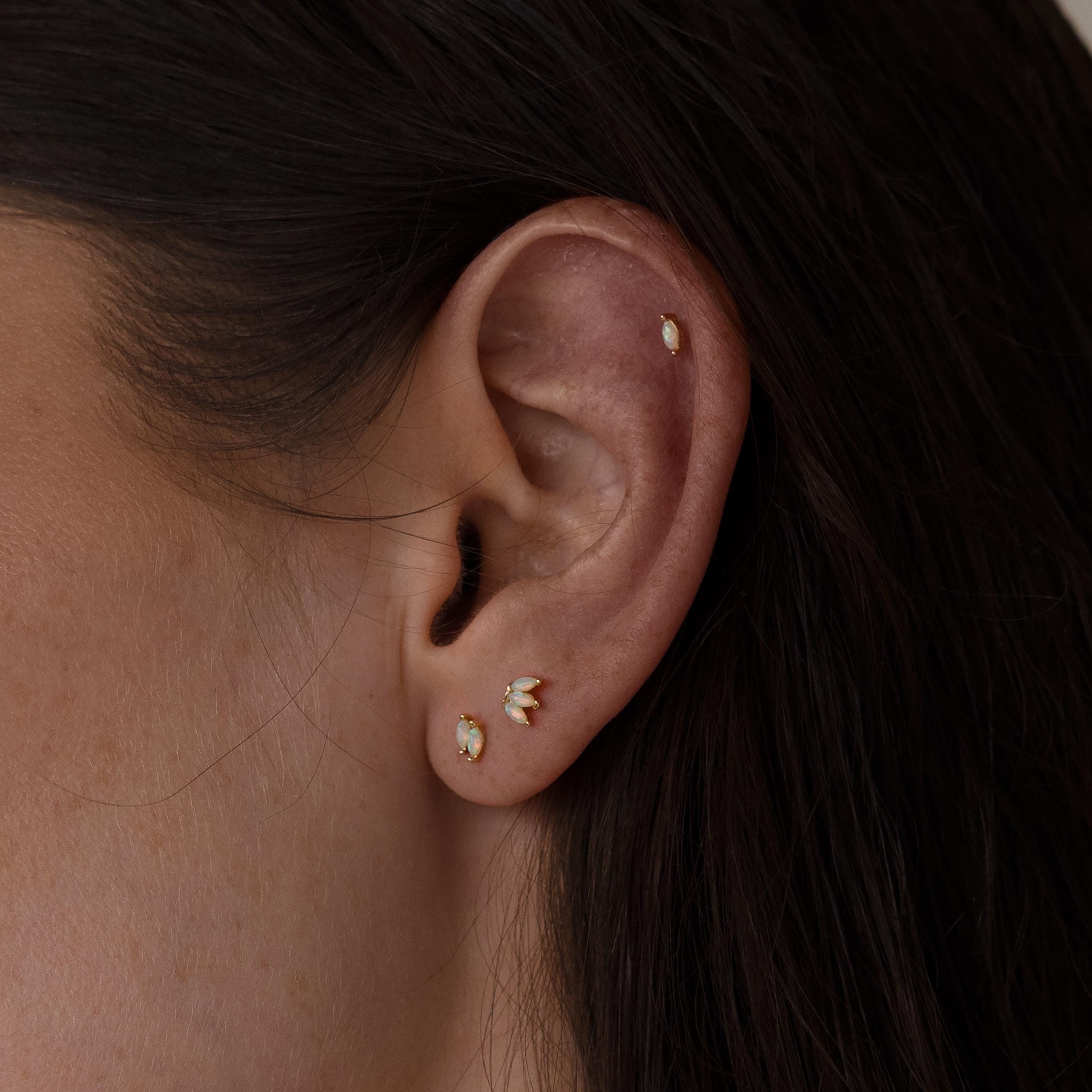 Close-up of a woman's ear with Marquise Opal Flat Back Studs—three gold and white gemstone earrings in the lobe and one in the cartilage, making a perfect Gift for Her.