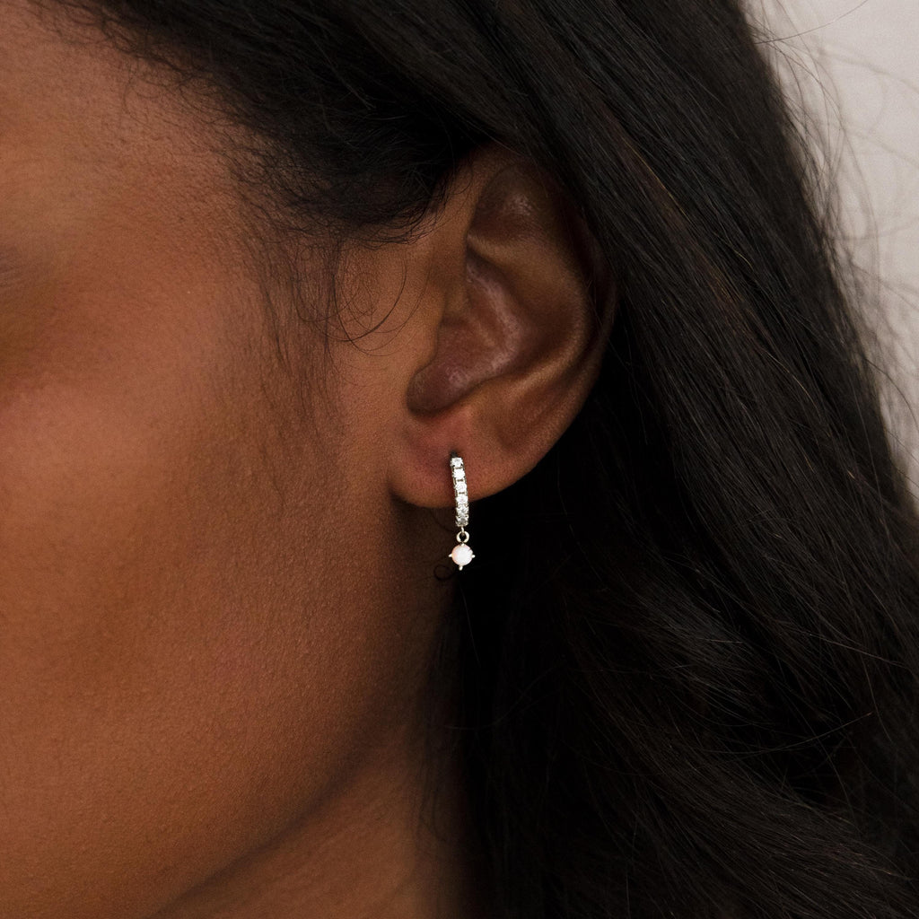 Close-up of a woman's ear wearing Pave Opal Drop Huggies—small silver hoops featuring dangling black and white beads.