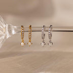 Two pairs of crystal-studded hoop earrings, including the gold Pavé Opal Drop Huggies and classic silver diamond earrings, are displayed on a glass rod.