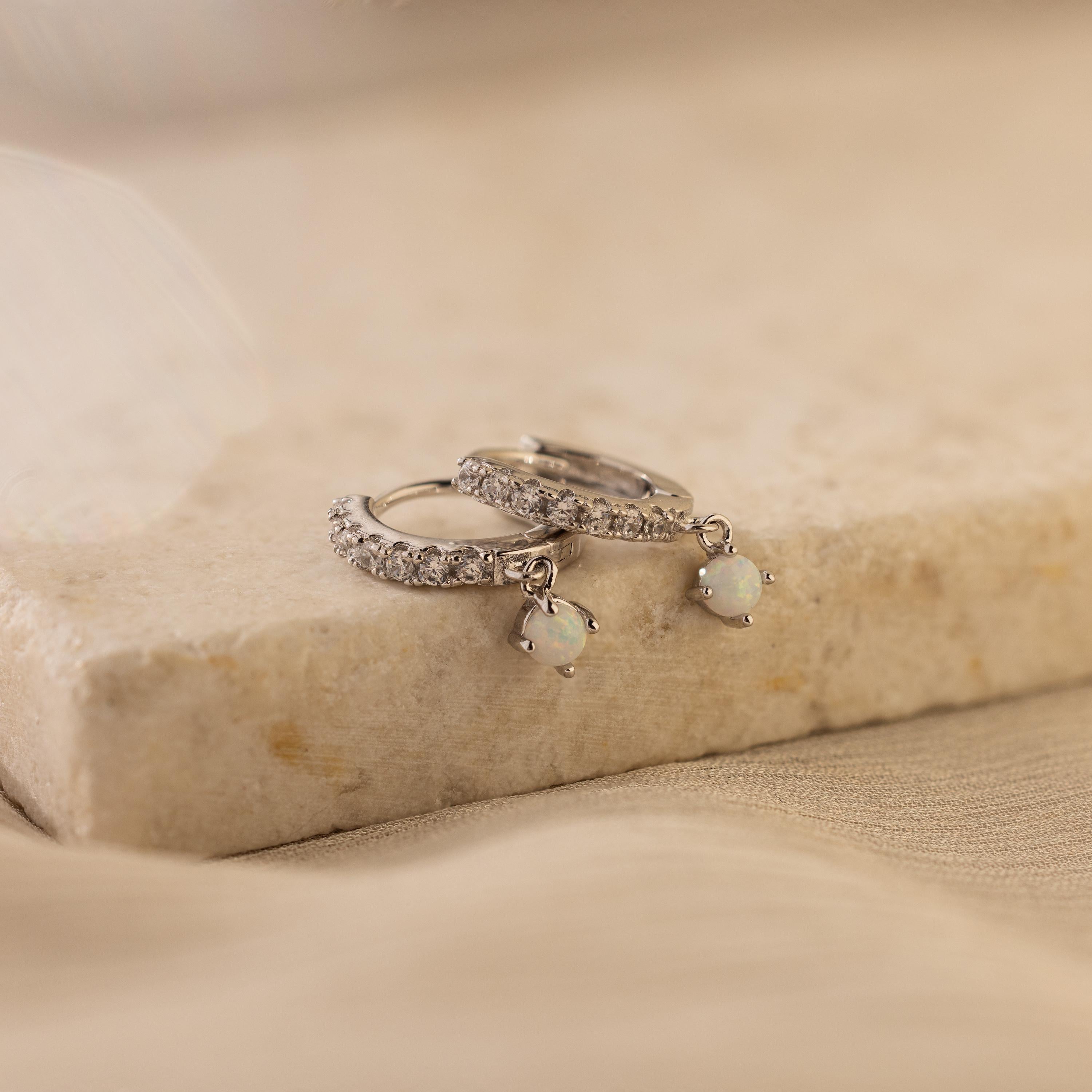 Pave Opal Drop Huggies in small silver, featuring sparkling pavé stones and dangling opal charms, displayed elegantly on a marble surface.