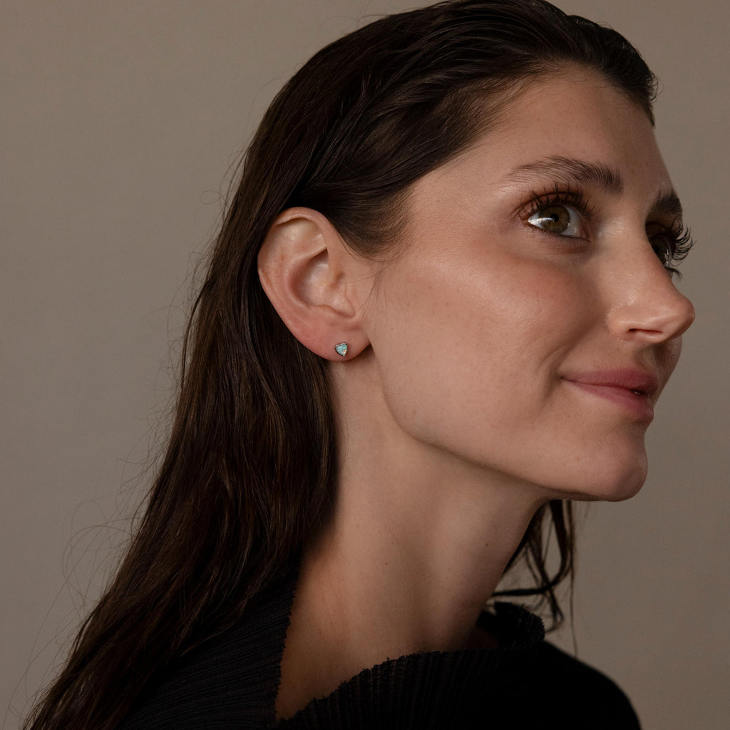 Woman with long brown hair, wearing a black top and Opal Heart Flat Back Studs, looks to the right.