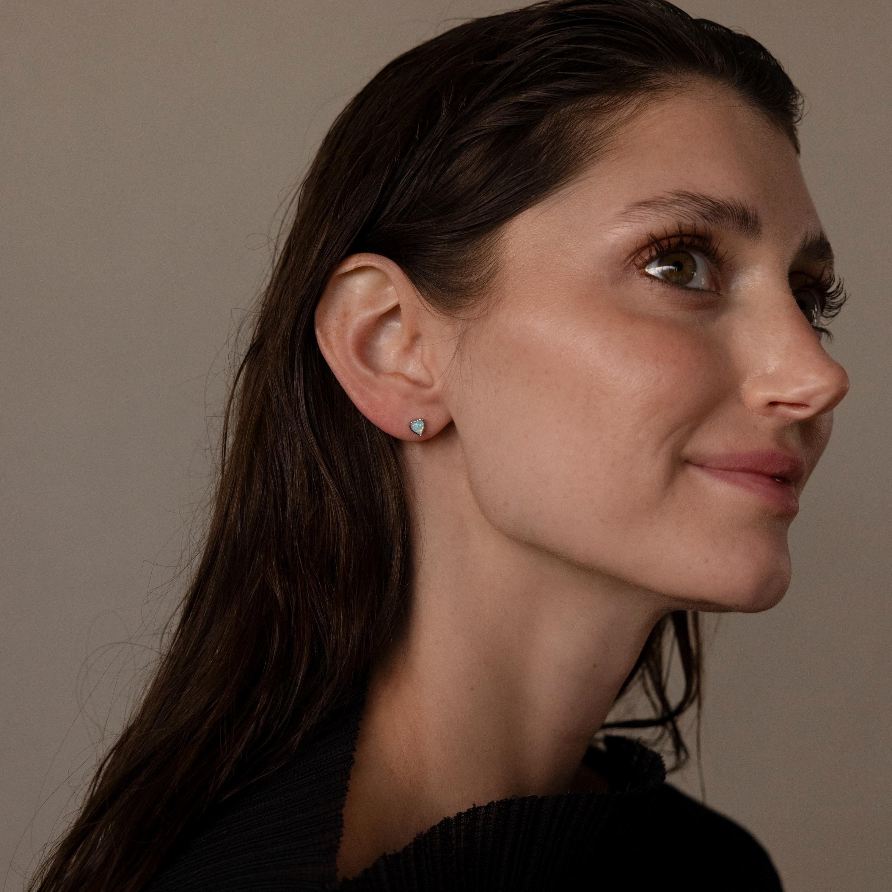 Woman with long brown hair, wearing a black top and Opal Heart Flat Back Studs, looks to the right.