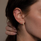 Close-up of a person's ear with three gold earrings, including Opal Heart Flat Back Studs, and their hand resting on the back of their neck.