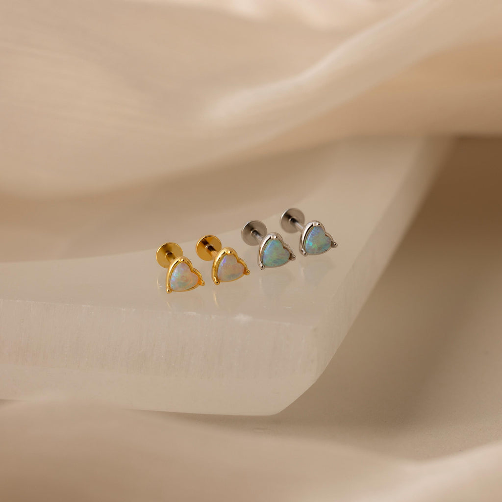 Two pairs of Opal Heart Flat Back Studs—one gold, one silver—are shown on a white surface, ideal for gemstone earring lovers or anyone wanting elegant birthstone jewelry.