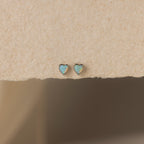 The Opal Heart Flat Back Studs are shown on a textured beige surface, offering a delicate addition to your gemstone earrings collection.