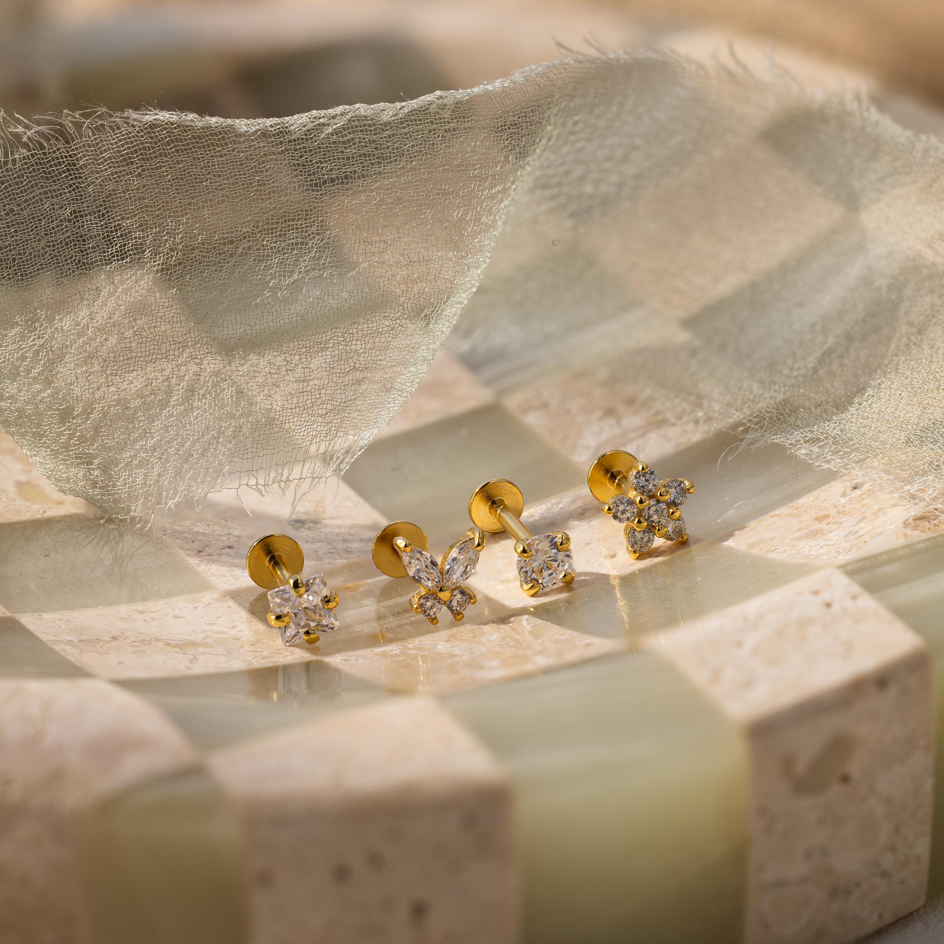 The Pave Assortment Flat Back Set features three pairs of gold and pavé diamond flat-back studs displayed on a checkered stone surface with sheer fabric above for an elegant presentation.
