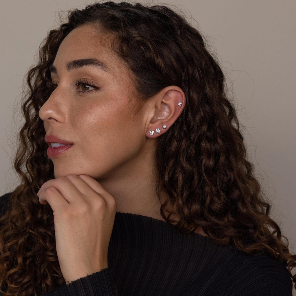 Woman with curly hair wears the Pave Assortment Flat Back Set, featuring silver earrings, as she looks to the side with her hand near her chin.