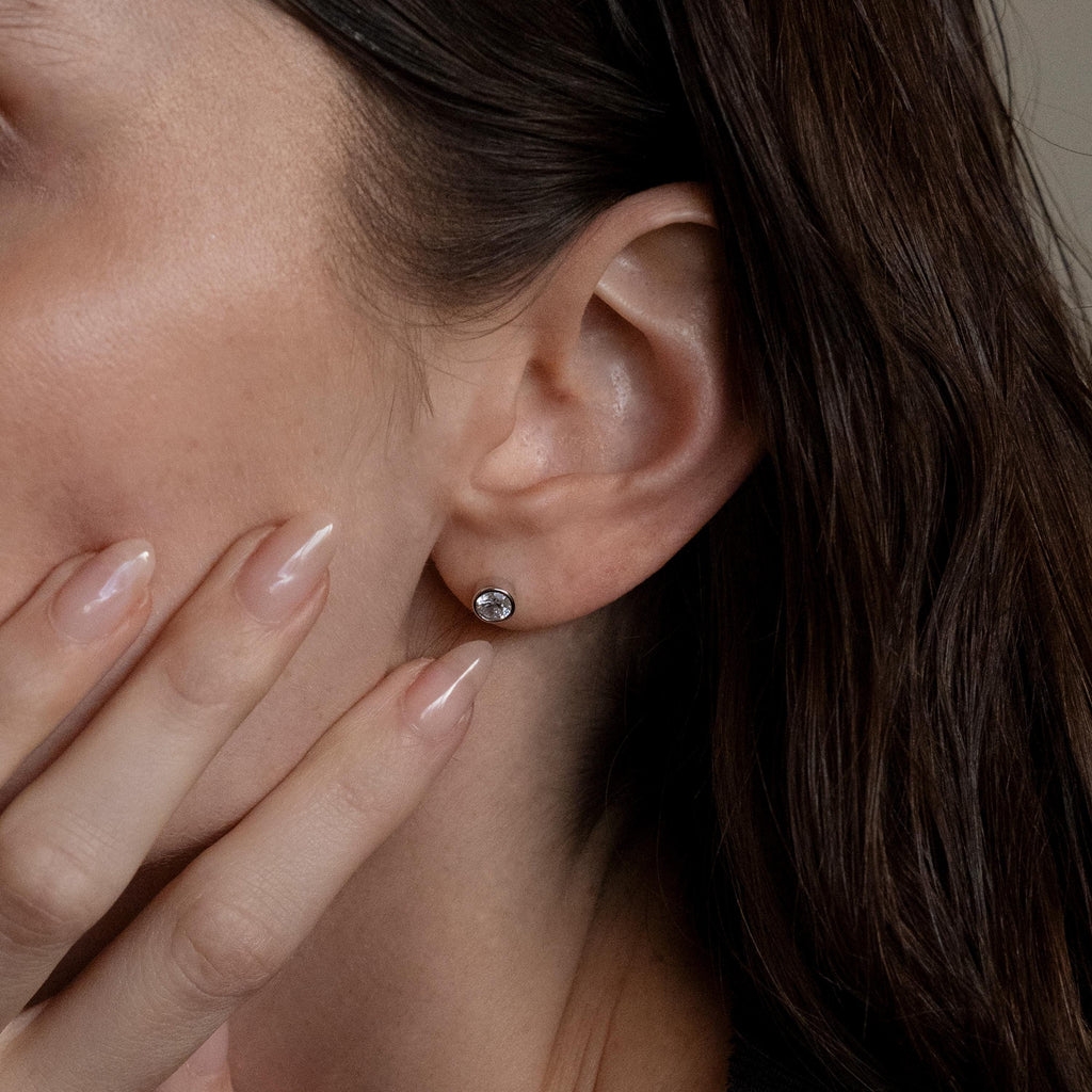 A close-up of a woman’s ear adorned with Large Diamond Bezel Flatback Studs as her hand gently touches her face.