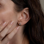 A close-up of a woman’s ear adorned with Large Diamond Bezel Flatback Studs as her hand gently touches her face.