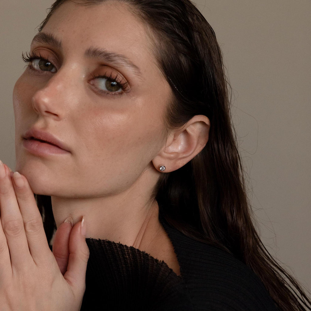 Woman with wet, dark hair wears a black top and Large Diamond Bezel Flatback Studs, gazing softly at the camera.