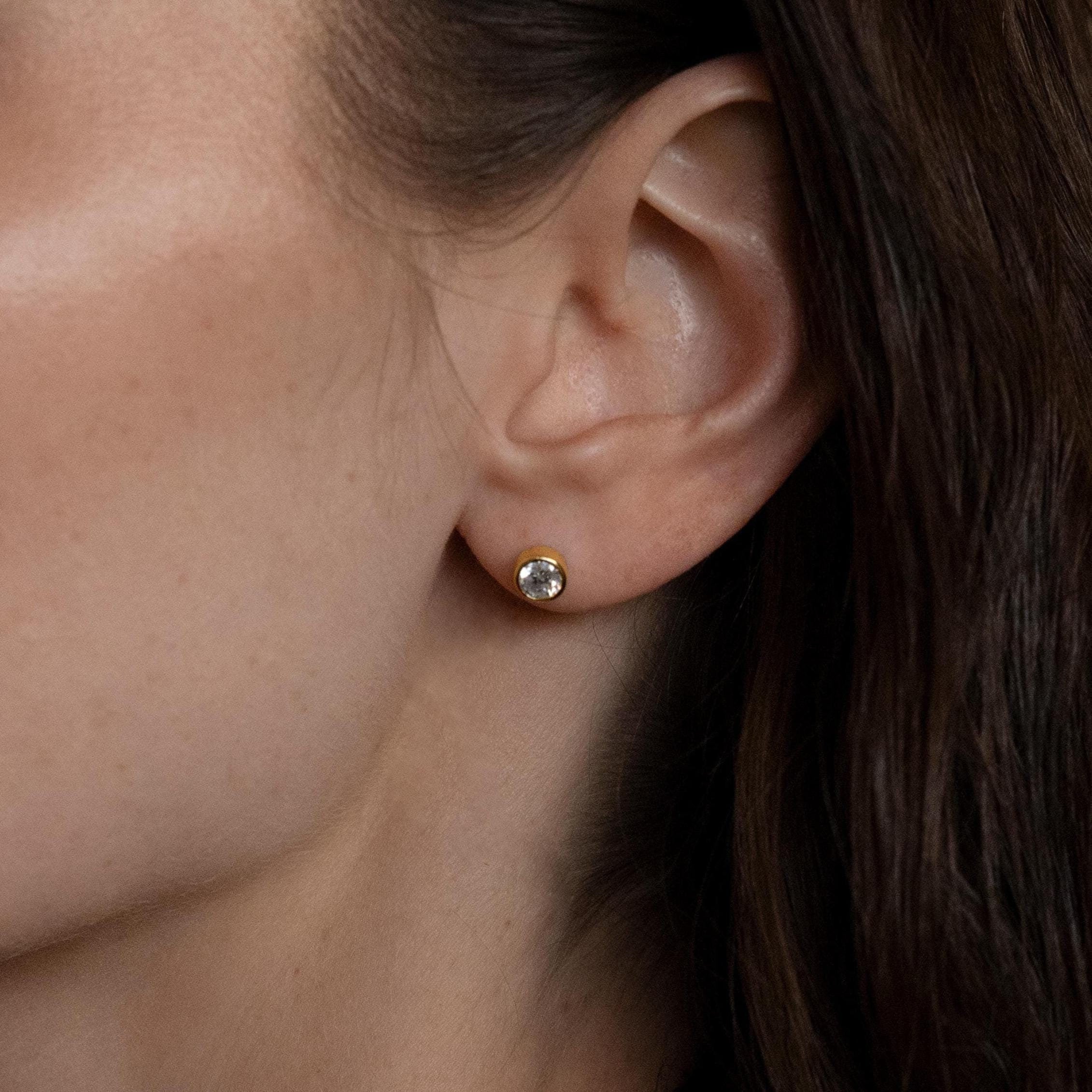 Close-up of a person's ear wearing Large Diamond Bezel Flatback Studs, featuring a round gold setting with a clear gemstone.